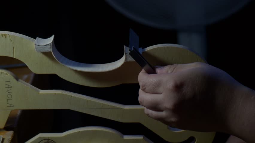 Violin rib edge being shaped on internal mold by luthier hand, refining curve and outline of new instrument body with controlled movement in traditional workshop environment, extreme close up shot.