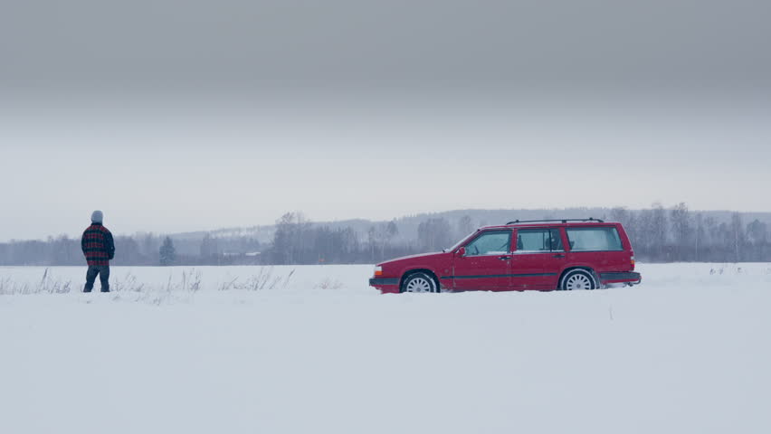 Man in front of idling red car with gases escaping exhaust in snowy landscape