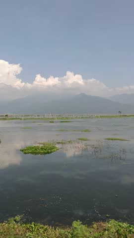 Calm lake landscape with mountain backdrop and cloud reflection on water under blue sky in natural outdoor scenery.