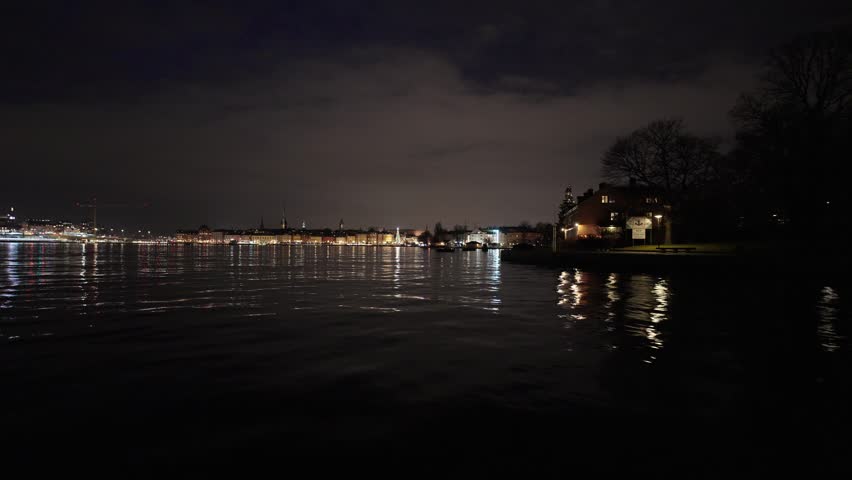 Stockholm, Sweden, a nighttime video from a moving boat on the water showing the illuminated city skyline, historic buildings, and a glowing Christmas tree at the harbor