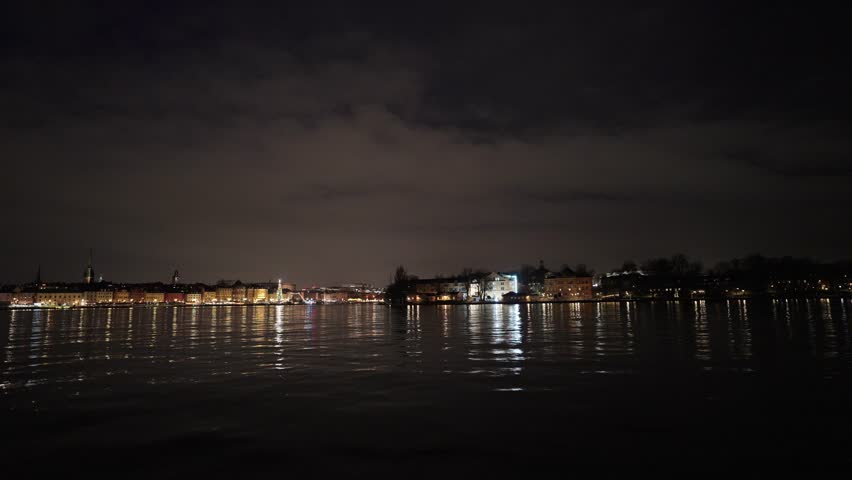 Stockholm, Sweden, a nighttime video from a moving boat on the water showing the illuminated city skyline, historic buildings, and a glowing Christmas tree at the harbor