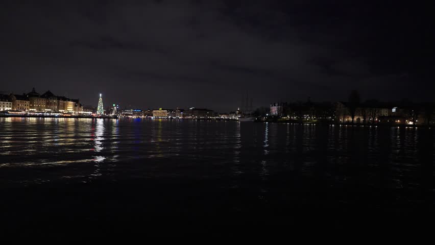 Stockholm, Sweden, a nighttime video from a moving boat on the water showing the illuminated city skyline, historic buildings, and a glowing Christmas tree at the harbor