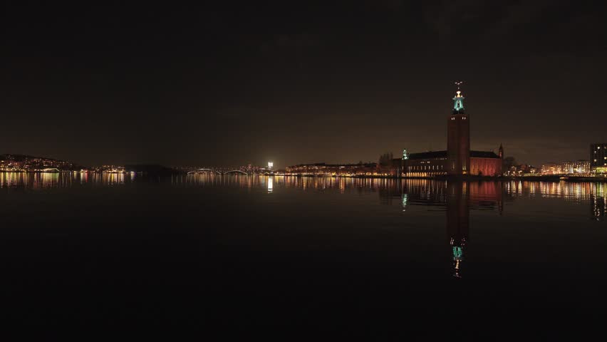 Nighttime video of Stockholm City Hall (Stadshuset) illuminated along the waterfront in Stockholm, Sweden, with golden reflections shimmering across calm water under a clear Nordic sky.