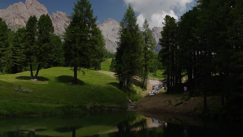 Footage of a peaceful mountain lake surrounded by trees, reflecting the serene natural beauty of the alpine landscape and calm waters under clear skies.