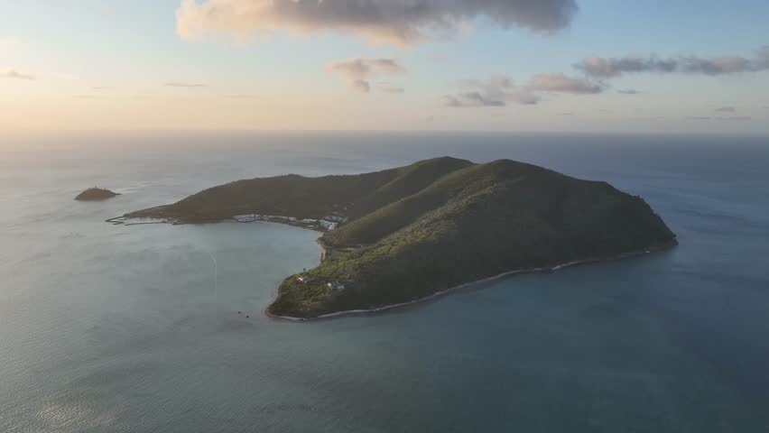 Smooth drone glide over Hayman Island at golden hour, showcasing the lush ridge line and sheltered bay surrounded by calm blue ocean in the Whitsundays, Queensland, Australia.