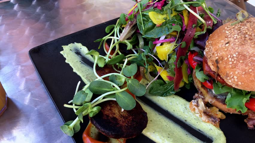 Bright vibrant side salad and gourmet hamburger on a black plate and dressing.