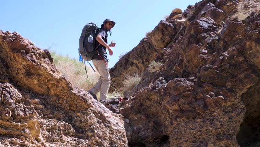 Male Hiker Standing In Between Rocks With Arms Open In Funny Gesture On The Ramon Crater Trail In Israel. Slow Motion, Zoom In