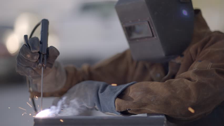 Side shot of person welding metal object while wearing protection mask