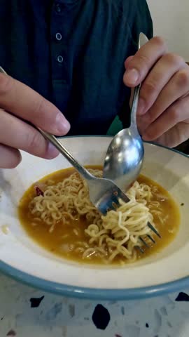 Close-up of gong zai mein or chicken instant noodles being eaten from a bowl with a fork and spoon, iconic staple cafe food in Hong Kong