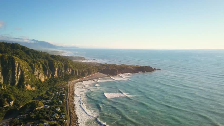Descent aerial view during golden hour of Punakaiki beach in New Zealand on a sunny summer day.