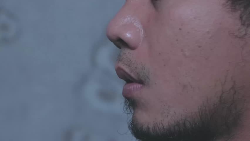 Side profile of a bearded man exhaling smoke from an electronic cigarette or vape.