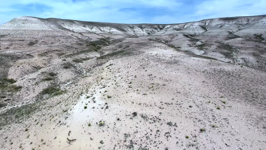Aerial view of barren limestone badlands, eroded hills and white soil in arid desert terrain. Overhead footage shows dry chalk landscape, rugged canyons, gullies, treeless wasteland slopes.