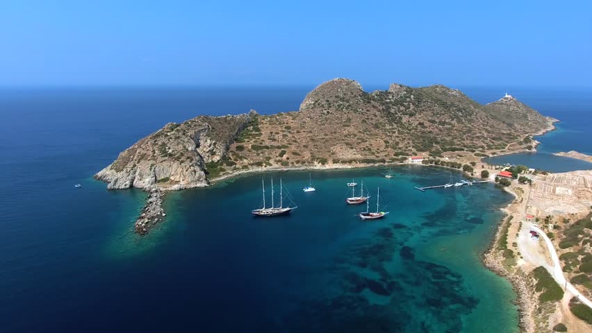 Aerial view of sailboats moored in turquoise harbor bay on Knidos Peninsula, Turkey. Overhead shot shows yachts anchored within a natural cove near Datca, Mugla, Aegean Mediterranean coast.