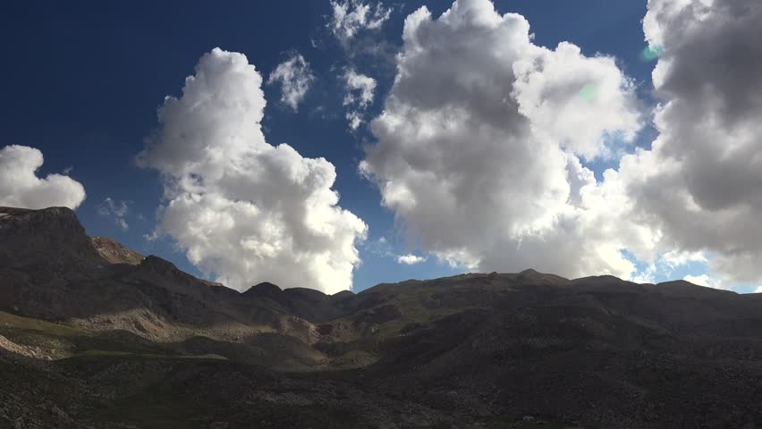 Panoramic cloudy Atlas Mountains landscape in Morocco with dramatic cumulus over dark ridges. Wide vista of Maghreb highlands under towering white clouds above rugged peaks and valleys at dusk.