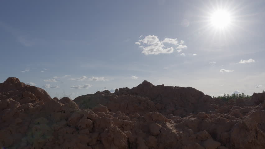Slow zoom out of vast arid landscape with high mounds of red soil under clear open afternoon sky, barren earth without vegetation, environmental or drought concept.