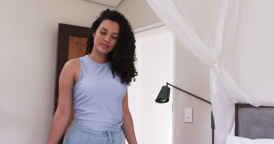 Adult woman in blue loungewear looking down, testing mattress, moving to lying seeking rest on bed. Bedroom, canopy, headboard, bedding, pillow, serenity, calm