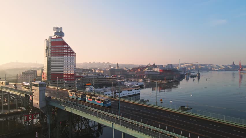 Tram Travelling At Gotaalvbron Bridge With P-Arken Ship On Harbour Beside Lilla Bommen Building At Sunrise In Gothenburg, Sweden. - aerial