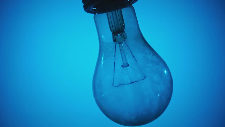 Close up of a glowing and fading light bulb on a bright blue background, symbolizing innovation and ideas.