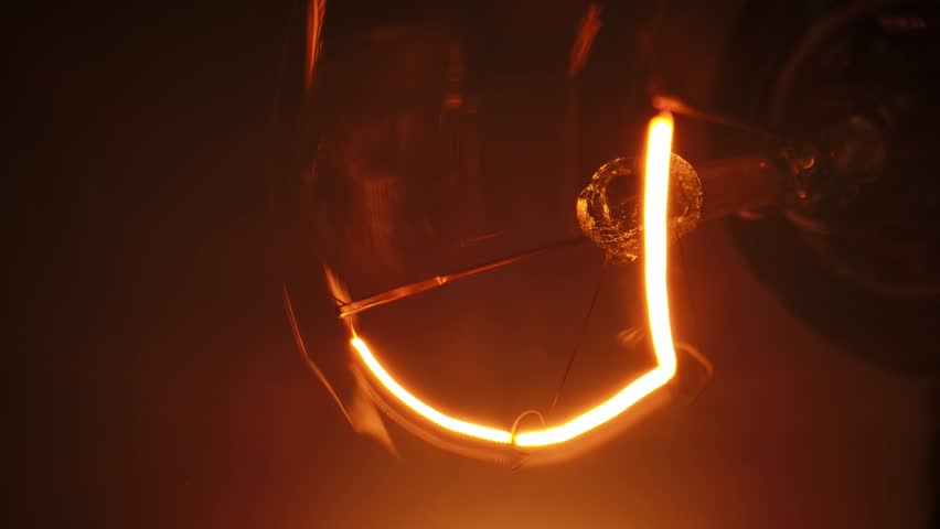 A detailed view of a glowing and fading light bulb filament in a dark setting, capturing warm and vibrant hues.