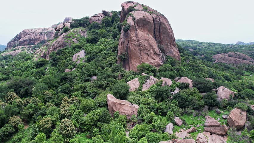 Aerial view of adventurers rock climbing and rappelling on Ramanagara Hill’s large rocky formation surrounded by rugged terrain and scenic natural landscape