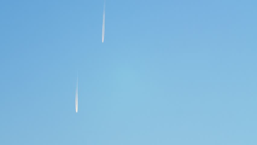 Two passenger planes are flying high in the sky, leaving a long white plume of fuel. Flying aircrafts high in the sky leaving a white trail.