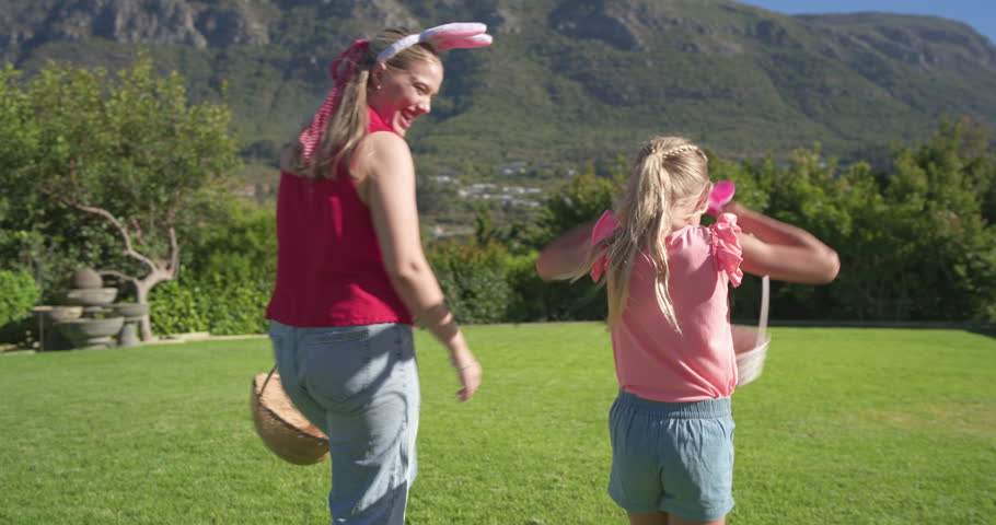 Mother and daughter turning walking lawn to fountain, searching basin with baskets and bunny-ears. Garden, backyard, pair, sunlit, mountains, hedge, waterfeature