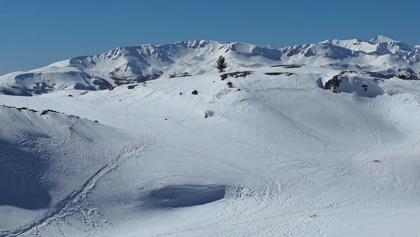 Snowy mountain peaks under clear blue sky, winter alpine landscape with fresh white snow and rocky ridges