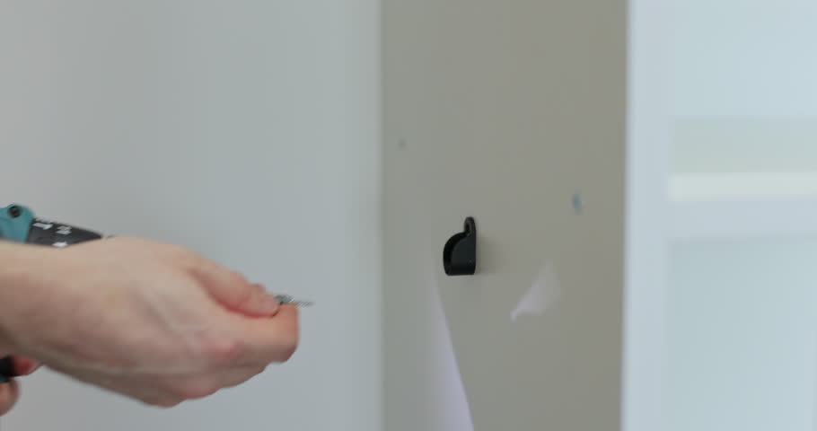 Man hands use electric screwdriver for installing screws into holes of shelf. Handyman engages in assembling process of modern prefabricated furniture.
