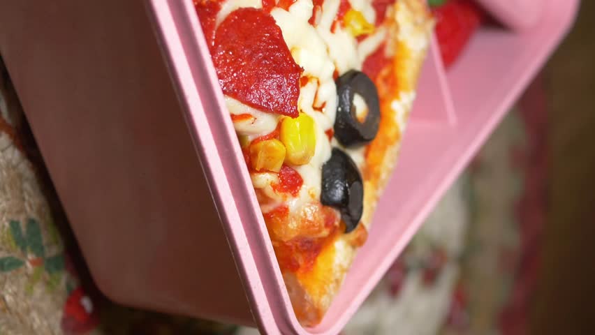 Healthy school lunch box with pizza slice and fresh strawberries in pink container on floral background