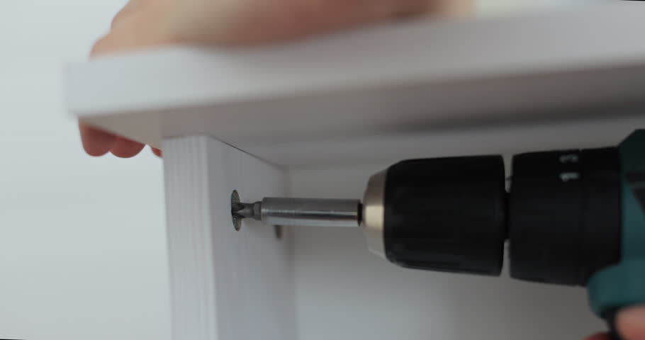 Close-up of person driving screw with cordless drill into furniture panel, assembling drawer.
