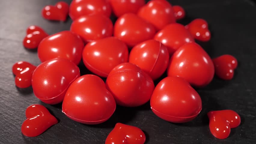 Close-up of several small, red decorative heart-shaped stress balls scattered on a dark wooden table. Smooth, shiny texture with bright color contrast.