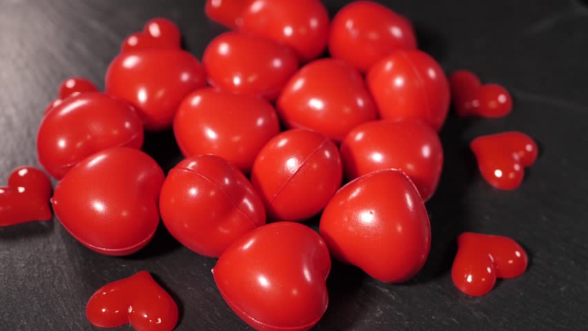 Close-up of several small, red decorative heart-shaped stress balls scattered on a dark wooden table. Smooth, shiny texture with bright color contrast.