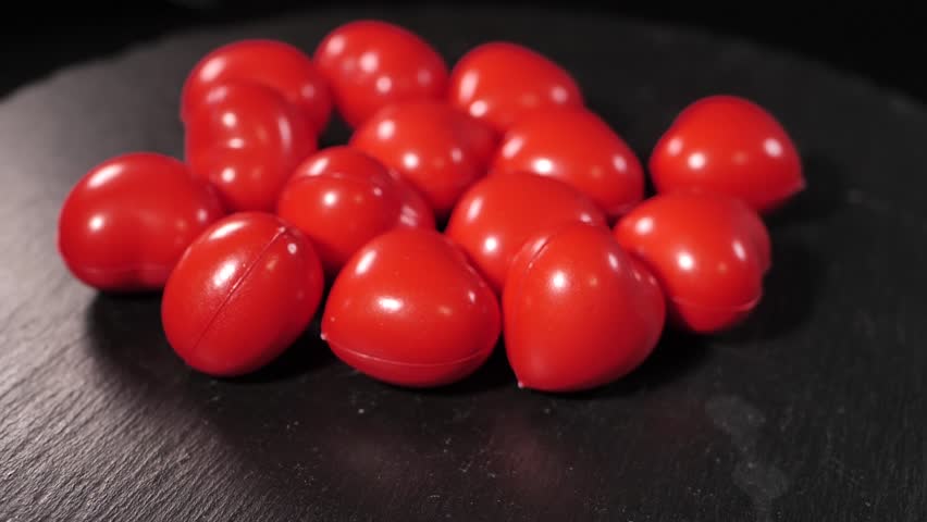 Close-up of several small, red decorative heart-shaped stress balls scattered on a dark wooden table. Smooth, shiny texture with bright color contrast.