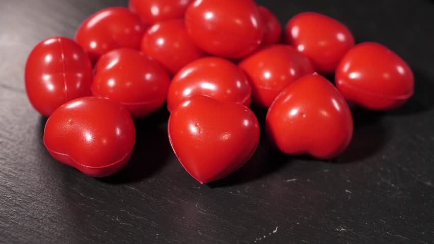 Close-up of several small, red decorative heart-shaped stress balls scattered on a dark wooden table. Smooth, shiny texture with bright color contrast.