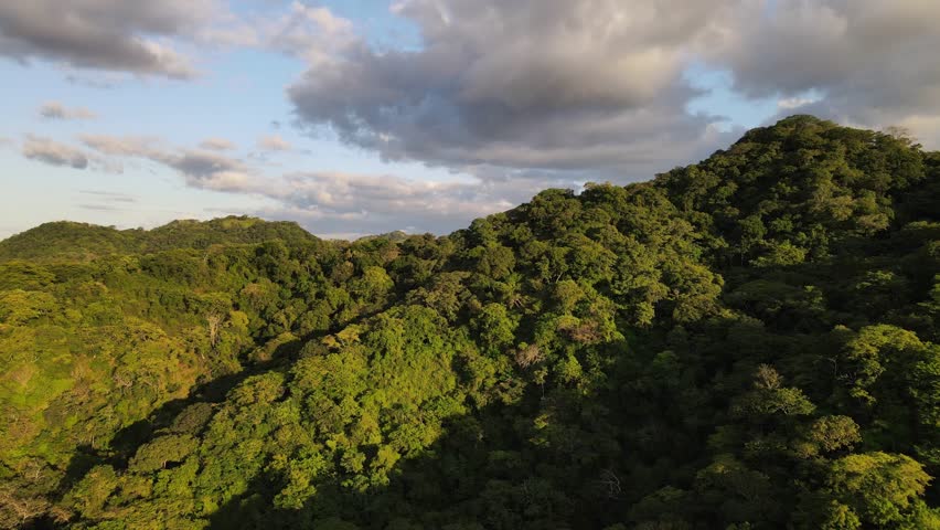 Dramatic sunset sky over the thick jungle of Costa Rica. Cinematic drone flight towards and above a ridge revealing a stunning and endless landscape dominated by forests and mountains.