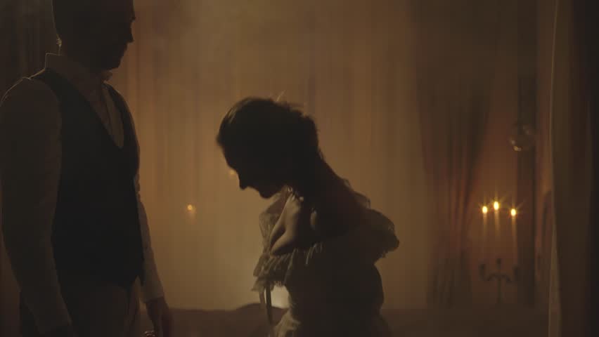 Black silhouette happy couple lady curtsies, gentleman kisses female hand. king greets queen victorian white dress. Night dark room candles light. Adult girl with man, love old style medieval ball 4k.