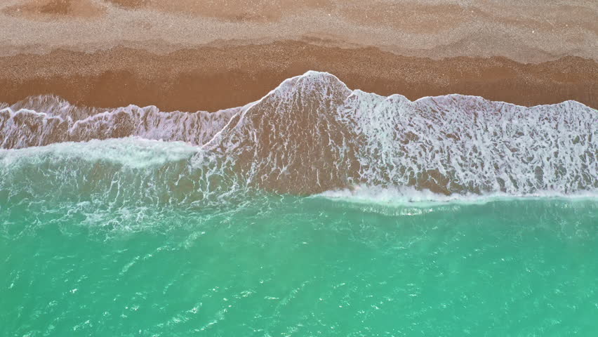 Cyprus beach with turquoise blue water meeting brown sand, foamy waves washing ashore, creating a beautiful natural contrast along the Mediterranean coastline from an aerial perspective, top down view