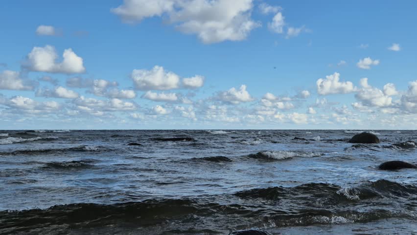 Choppy waves under bright daylight and scattered clouds. Natural ambient sea sound included. Detailed 4K seaside landscape footage.