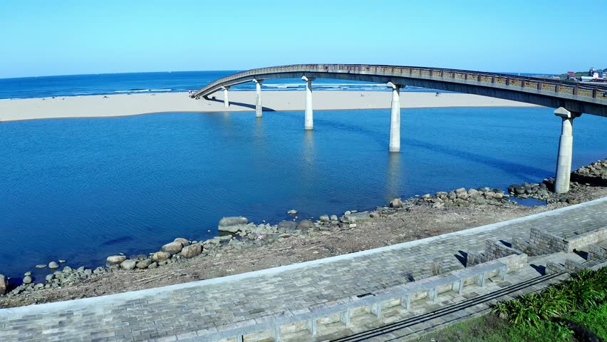 Aerial flight under water bridge and over sandy Fulong Beach in Taiwan during blue sky