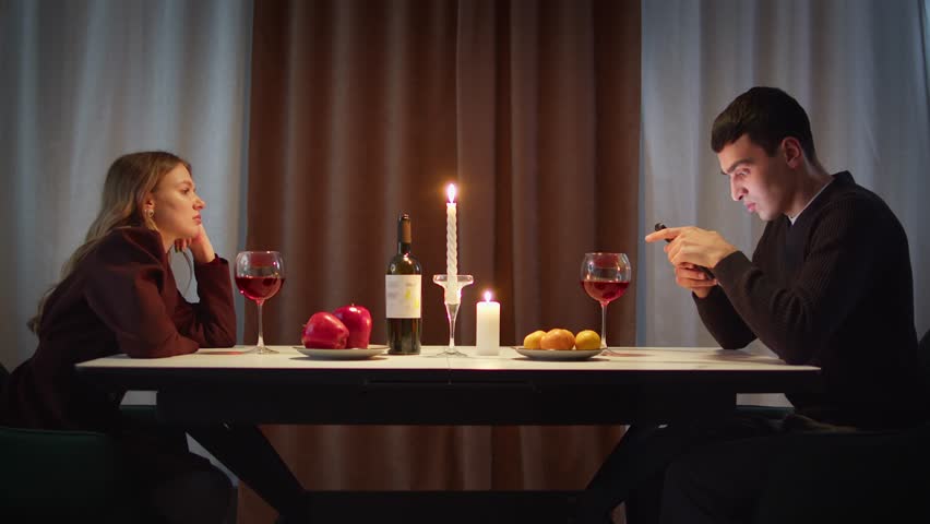Couple with cell mobile phone addiction having evening wine dinner together. People celebrating event. Awkward ignore romantic first date problem at restaurant or home. Holiday candle light atmosphere
