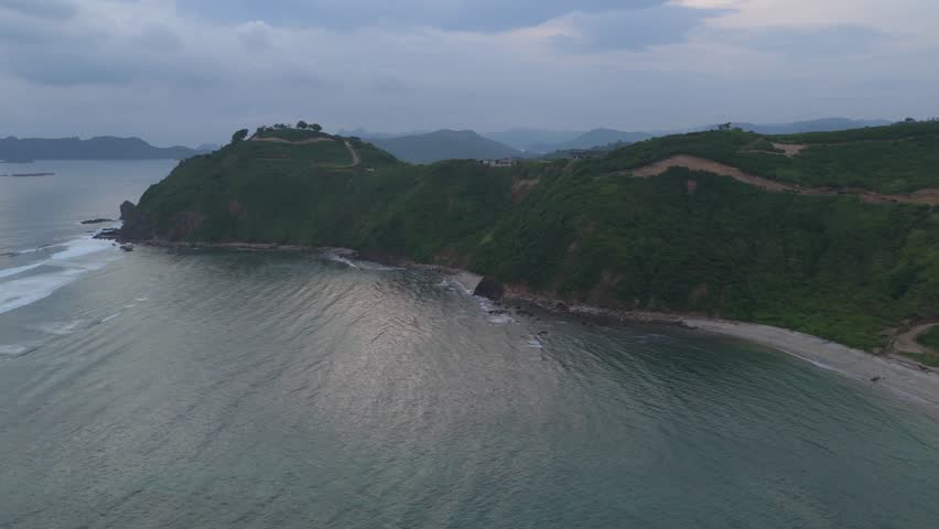 Aerial perspective of rugged coastal hill and bay with textured water and dramatic natural contours