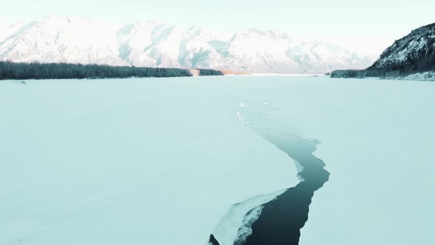 Stunning 4K aerial footage of the Knik River flowing through the breathtaking winter landscape near Palmer, Alaska, captured in 2021. This cinematic drone video showcases snow-covered riverbanks, frozen textures, and the dramatic contrast between icy terrain and winding water channels. Surrounded by vast wilderness and towering mountain backdrops, the scene highlights the raw beauty and untouched serenity of Alaska in winter.