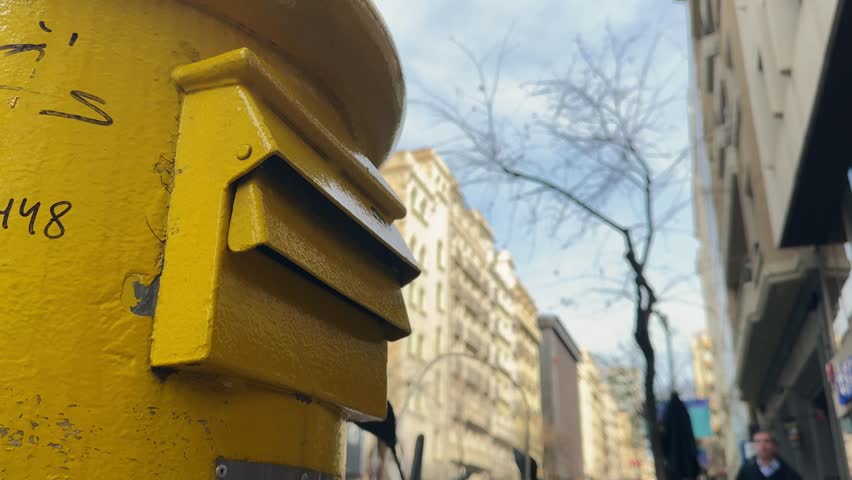A person drops a letter into a mailbox on the street. The mail is being sent, with cityscapes visible in the background.