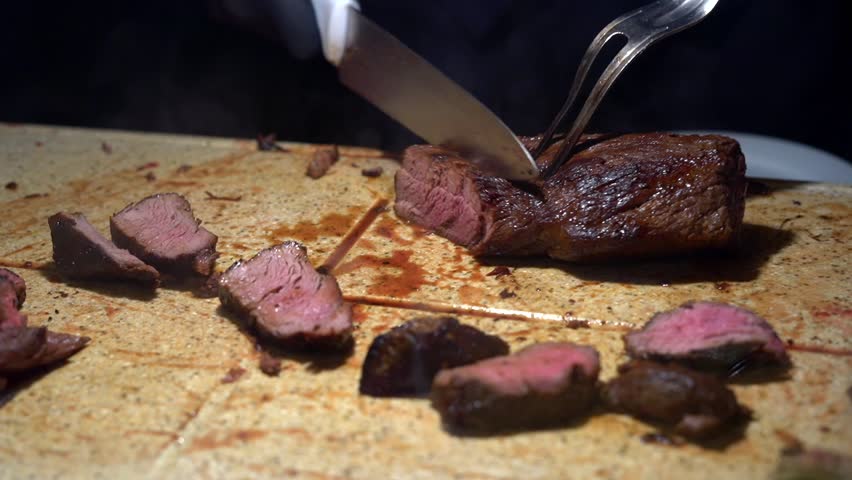 A chef cuts a tenderloin steak on a board at a luxury party buffet.