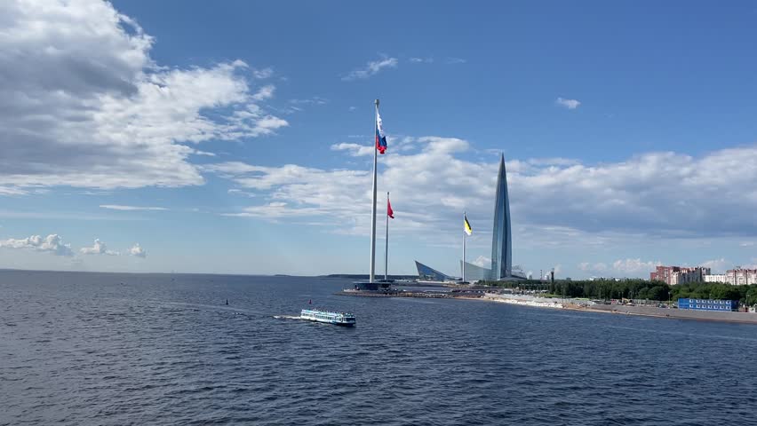 A scenic sightseeing boat filled with tourists gracefully cruises past the iconic Lakhta Center skyscraper in St. Petersburg, Russia. The modern high-speed passenger vessel, equipped with comfortable seating and large panoramic windows, glides across the calm waters of the Gulf of Finland, offering passengers a unique view of Europe