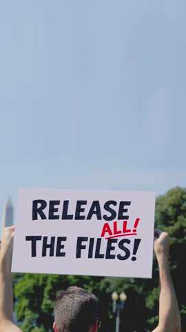 Vertical view of a person holding “Release All The Files” protest sign in front of the White House. Political demonstration scene with government building in background. 15046