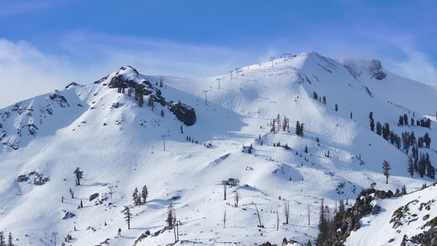 Winter sports action as skiers and snowboarders ride down steep mountain slope in Palisades Tahoe, California USA. Powerful alpine movement with snow covered terrain.