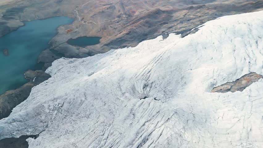 A spectacular high-angle aerial parallax shot sweeps over the vast Pastoruri Glacier, revealing its textured ice field and the deep blue glacial lakes formed by its meltwater in the Andes.