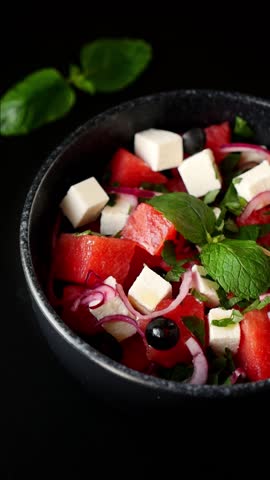 Healthy summer watermelon salad with feta, mint, and onion in black bowl, fresh and refreshing dish.
