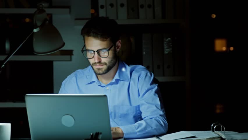 Man typing laptop, causing blue cart lock nodes passing around him, monitoring ecom security. Office, night, workstation, desk, computer, keyboard, overlay